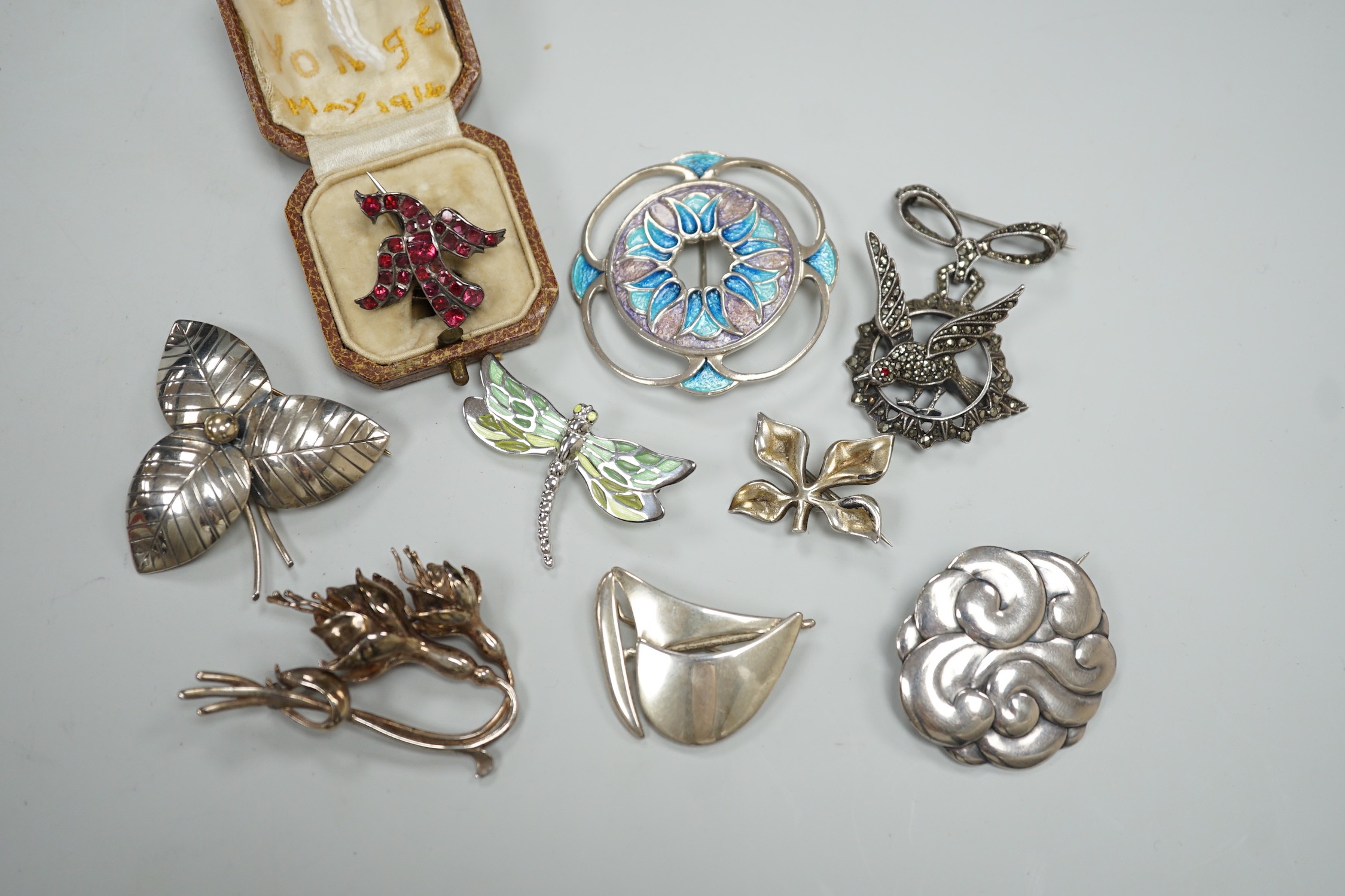 An early 20th century white metal and foil backed garnet cluster set bird brooch, 27mm and eight other assorted mainly 925 brooches including two enamelled and one Finnish yacht brooch.
